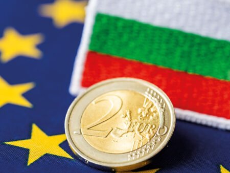 Монета в 2 евро на фоне флагов ЕС и Болгарии