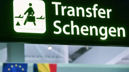 Указатель "Transfer Schengen" в аэропорту на фоне флагов ЕС и государств-членов