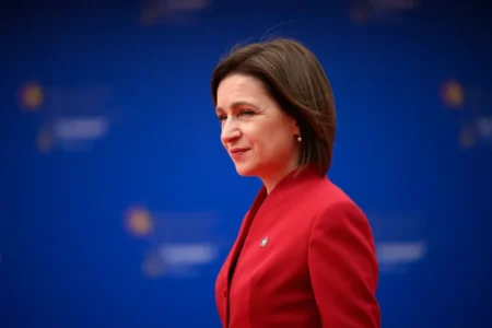 Президент Молдовы Майя Санду в красном костюме на фоне синего экрана