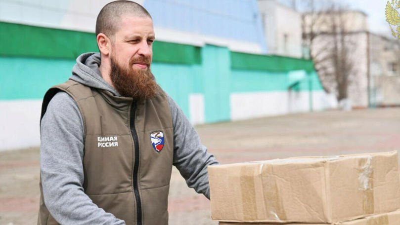 Мужчина с коробками в жилетке с эмблемой “Единая Россия” на улице