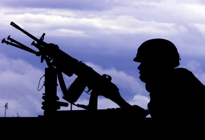 Силуэт вооружённого солдата на фоне облачного неба