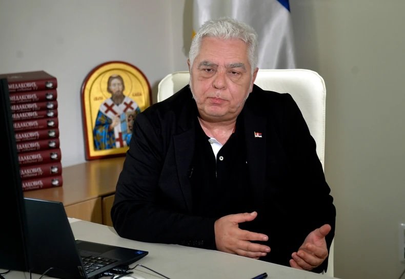 Борис Братина за рабочим столом с ноутбуком, на фоне православная икона и стопки книг