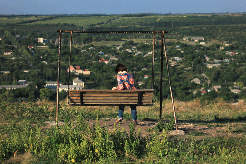 Девушка на деревянных качелях смотрит на панораму молдавского села в долине с холма