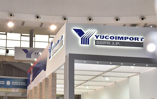 Выставочный стенд компании Yugoimport SDPR с логотипом на фоне баннеров с гербом Сербии и надписью Republic of Serbia Ministry of Defence
