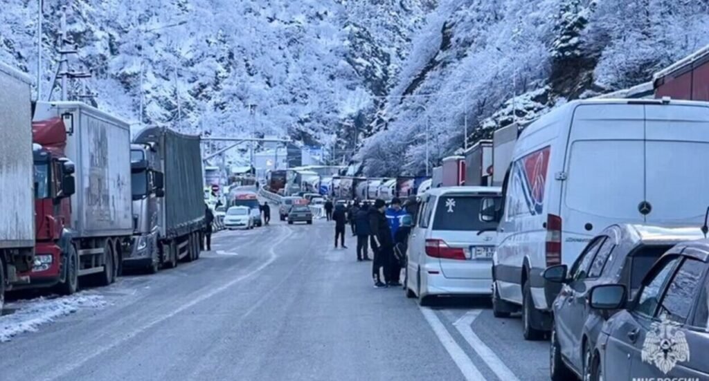 Очередь из грузовиков и легковых автомобилей на Военно-Грузинской дороге в зимних условиях, заснеженные горы на фоне