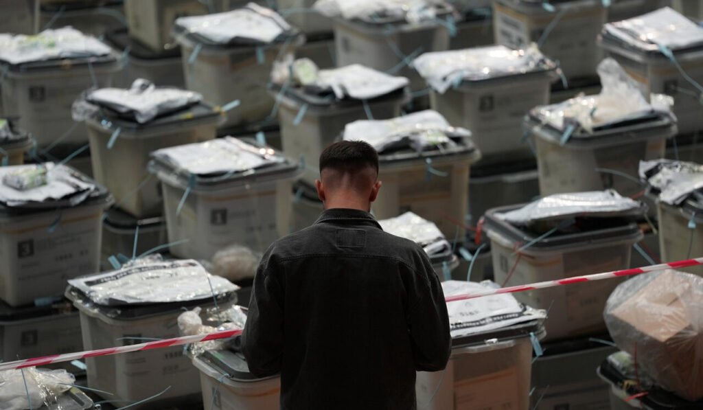 Сотрудник избирательной комиссии Косово перед рядами запечатанных урн в Центре подсчёта голосов