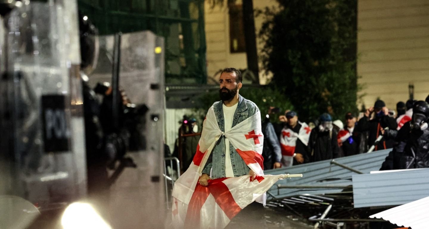 Мужчина с грузинским флагом стоит перед полицейским оцеплением во время протестов в Тбилиси