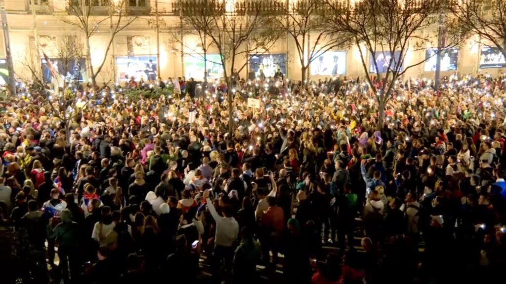 Огромная толпа протестующих в центре Белграда вечером 15 марта 2025 года, многие держат телефоны с включенными фонариками