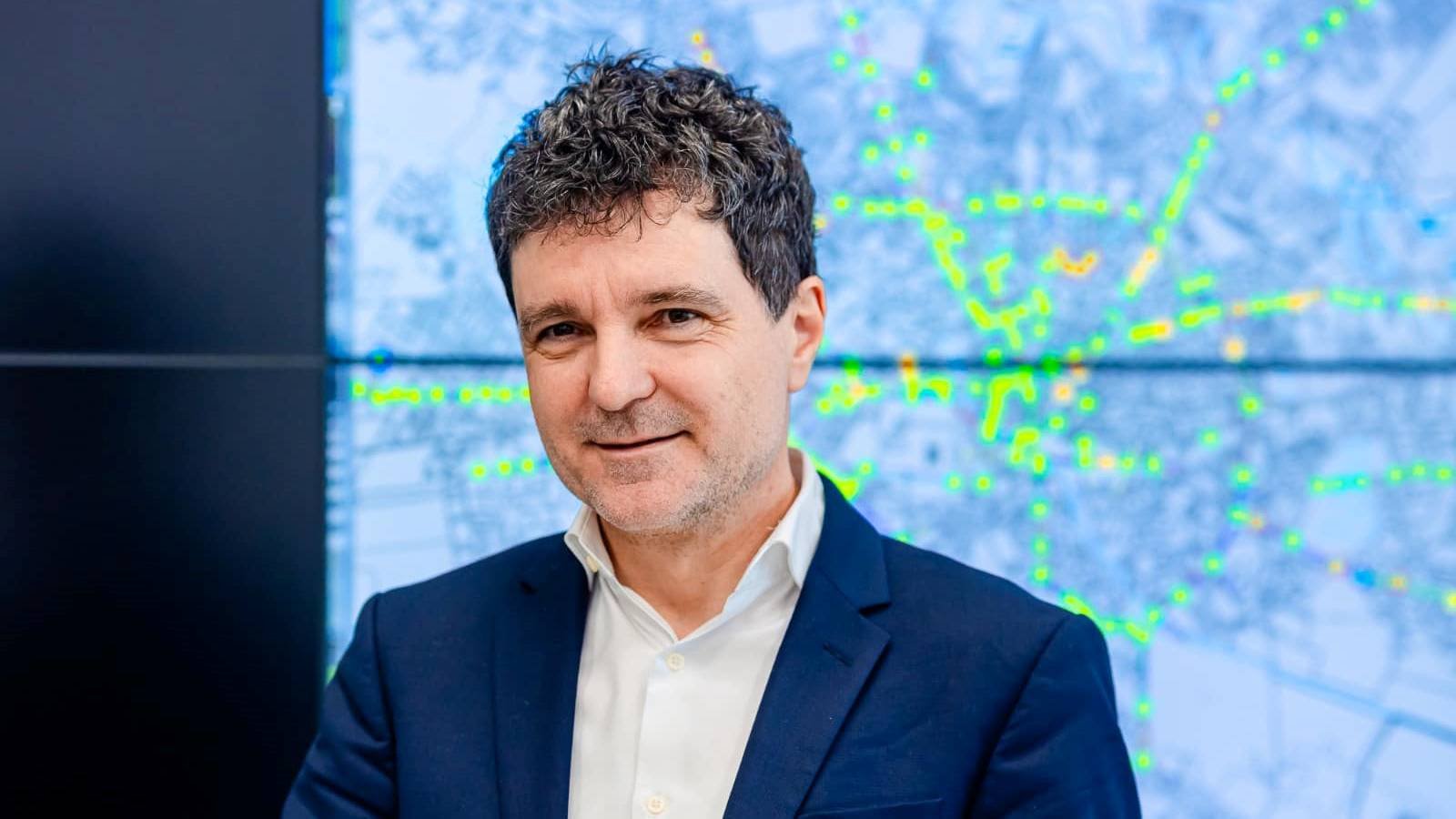 Президент Румынии Никушор Дан в деловом костюме на фоне экрана с информационной графикой