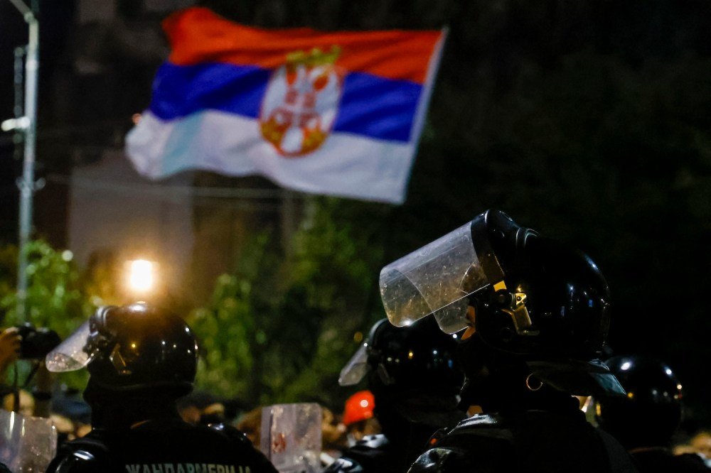 Сербские полицейские в шлемах на фоне развевающегося флага Сербии во время ночных протестов в Белграде, январь 2026
