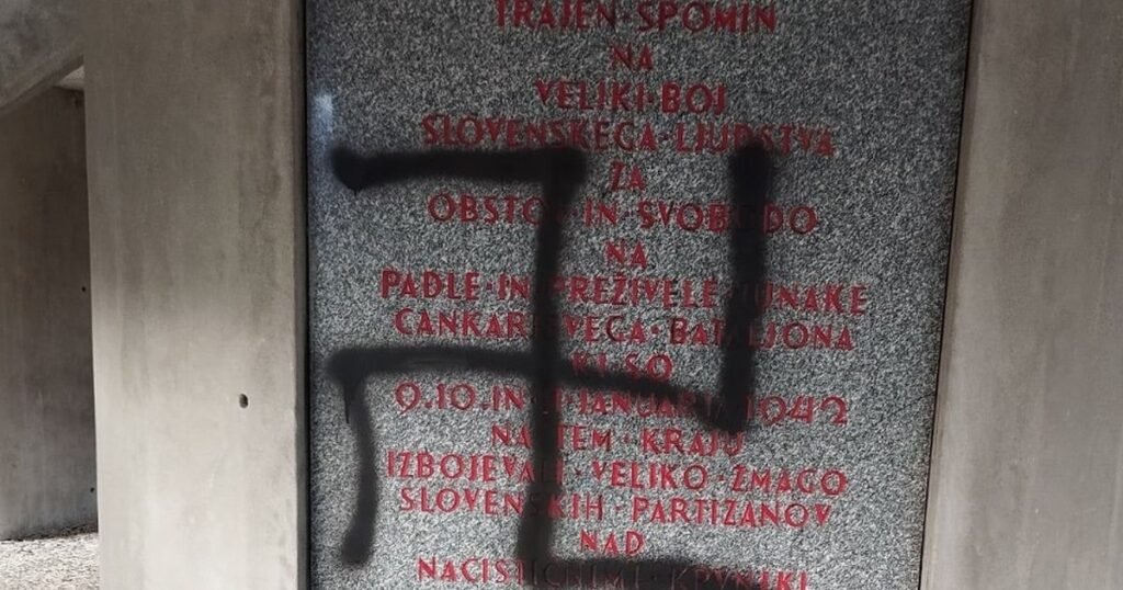 Крупный план оскверненной мемориальной плиты со свастикой, нарисованной поверх красного текста в память о словенских партизанах