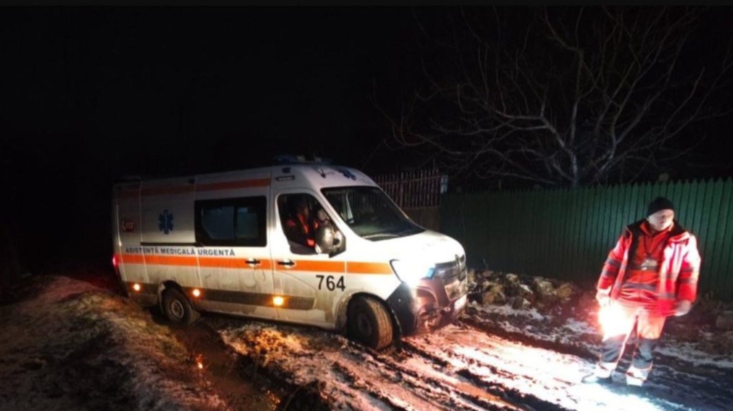 Скорая помощь №764 застряла на обледеневшей грязной дороге ночью, рядом стоит фельдшер