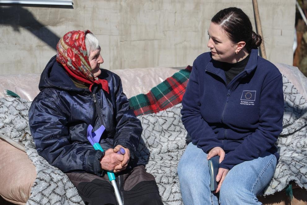 Сотрудница гуманитарной миссии ЕС беседует с пожилой женщиной в платке, демонстрация личной гуманитарной поддержки
