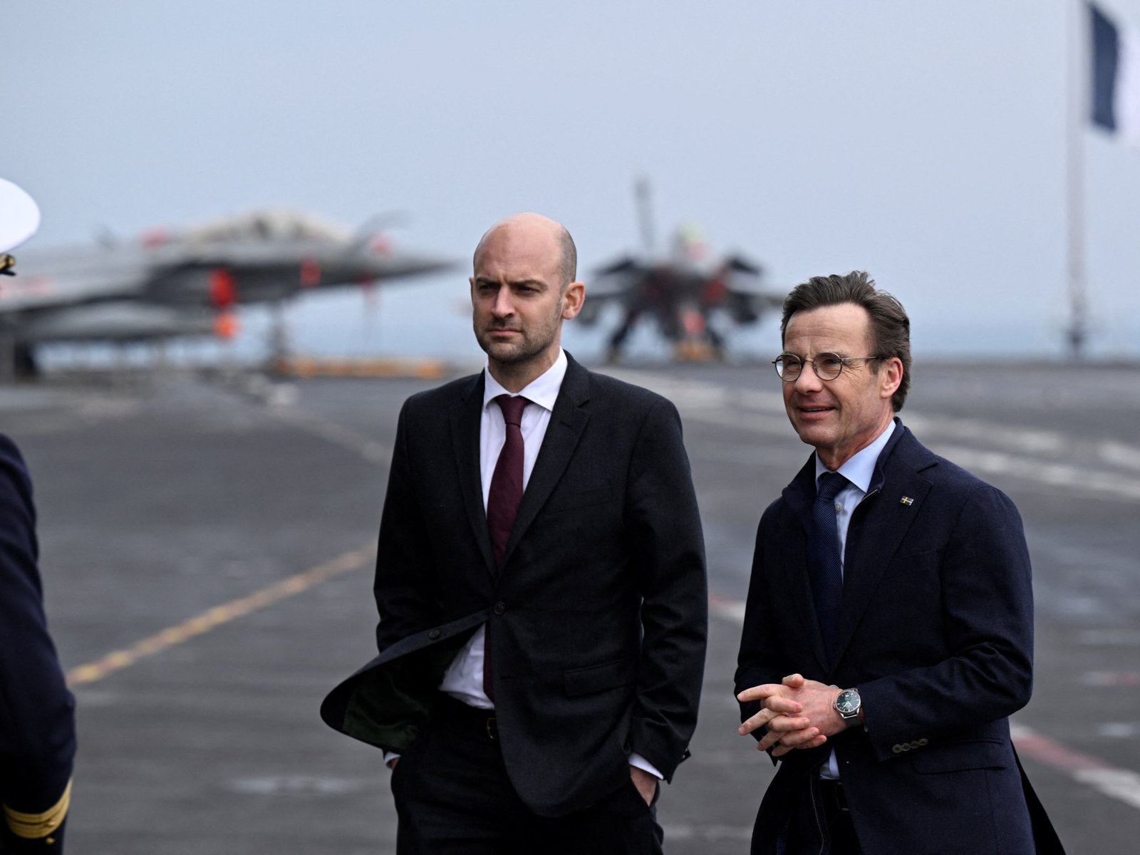 Swedish officials visiting the carrier deck with Rafale jets visible in background