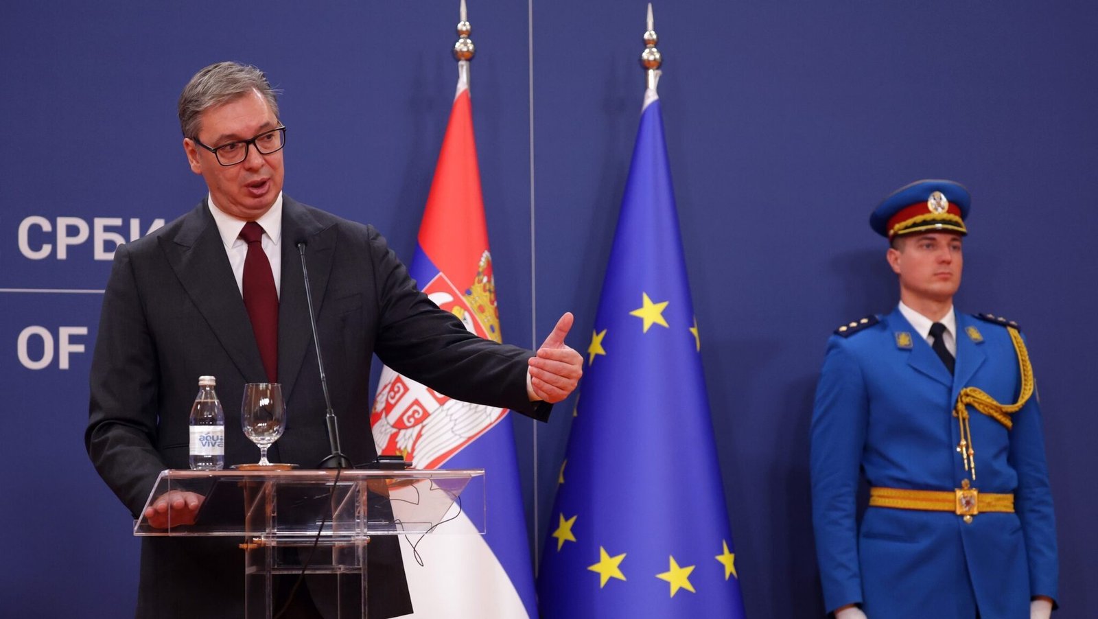 Serbian President Aleksandar Vučić speaking at a podium with Serbian and EU flags