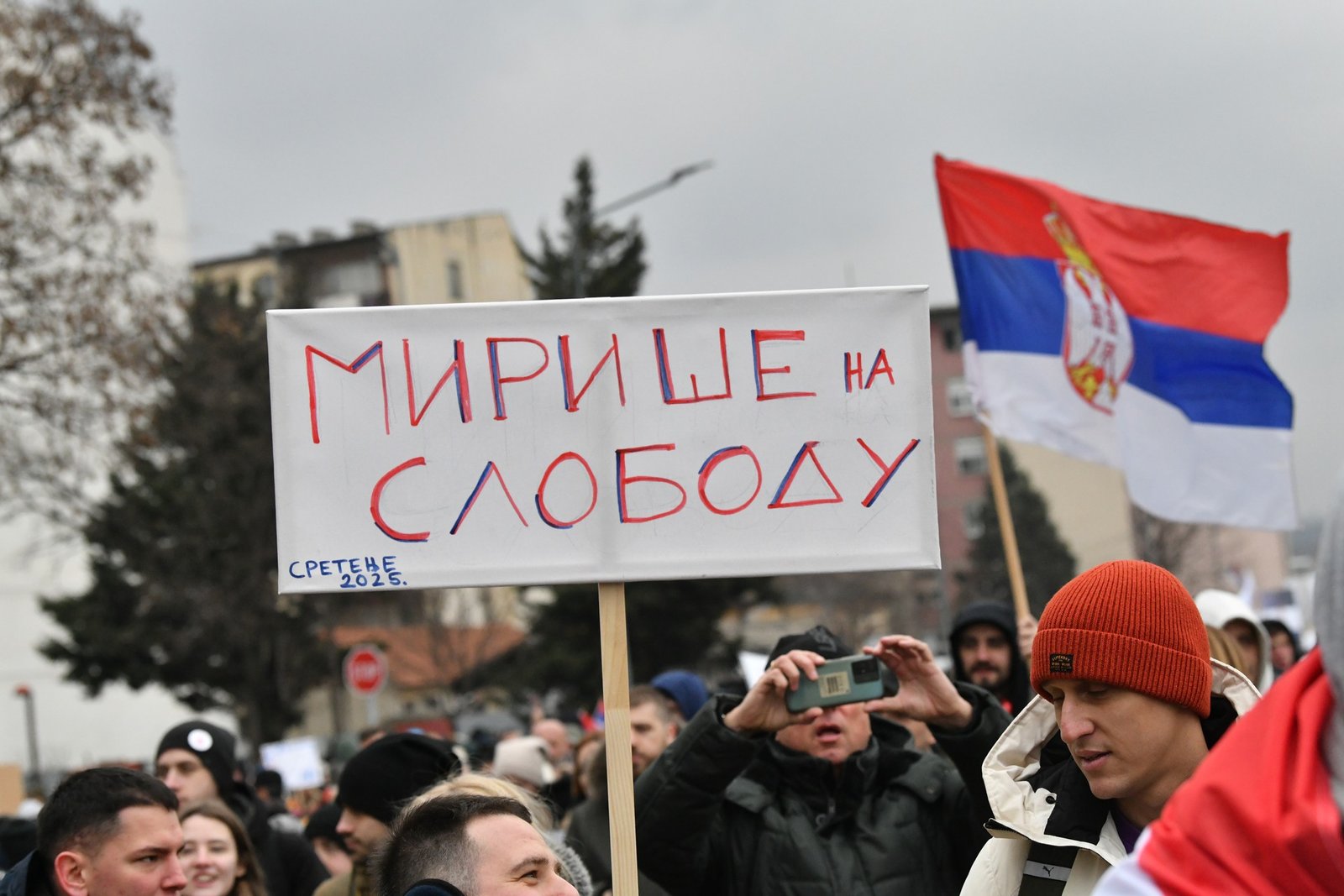 Участник протеста с плакатом «Мирише на слободу» и сербским флагом — акция «Сретнимо се поново», Сретенье 2025. Фото: Nova.rs