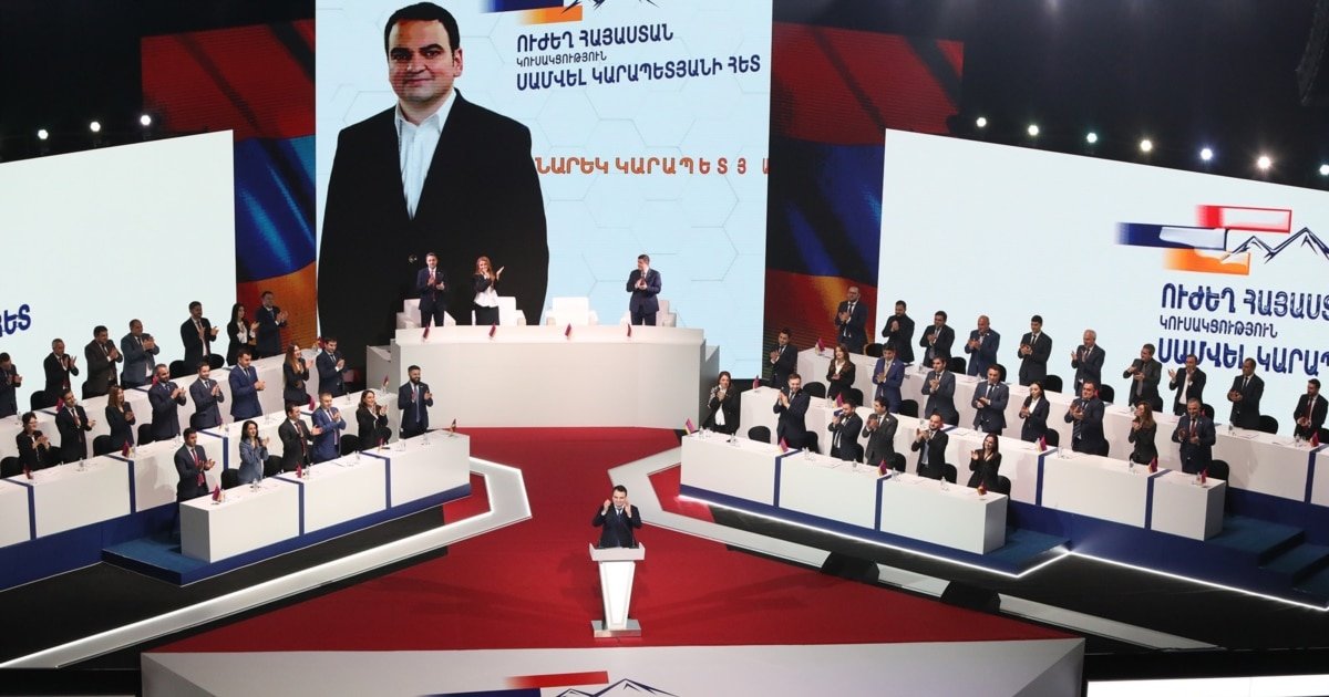 Съезд партии «Сильная Армения» — Нарек Карапетян выступает на трибуне, на экране портрет Самвела Карапетяна. Фото: JAM-News