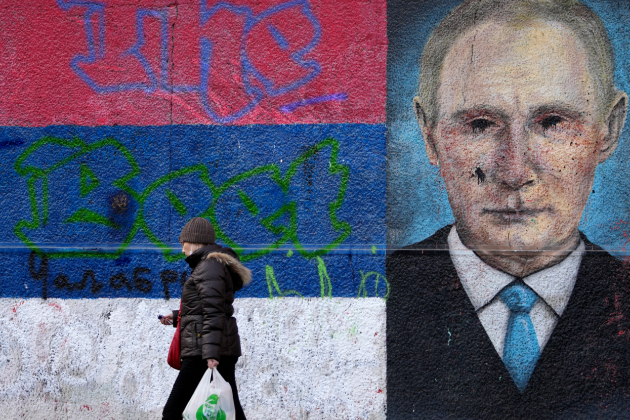 Женщина проходит мимо граффити с Путиным на стене с сербским флагом в Белграде