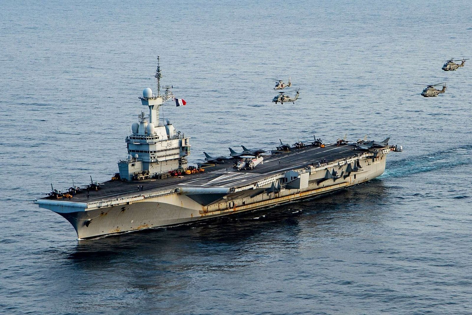 Charles de Gaulle aircraft carrier underway at sea with helicopters flying overhead