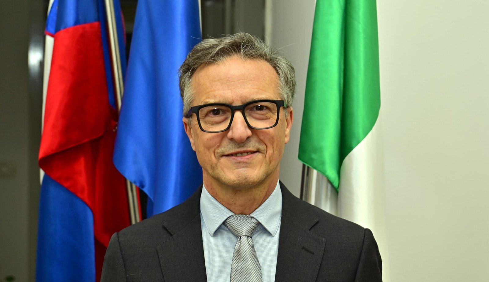 Портрет Феличе Жижи, представителя итальянского национального меньшинства в Словении, на фоне флагов Словении, ЕС и Италии