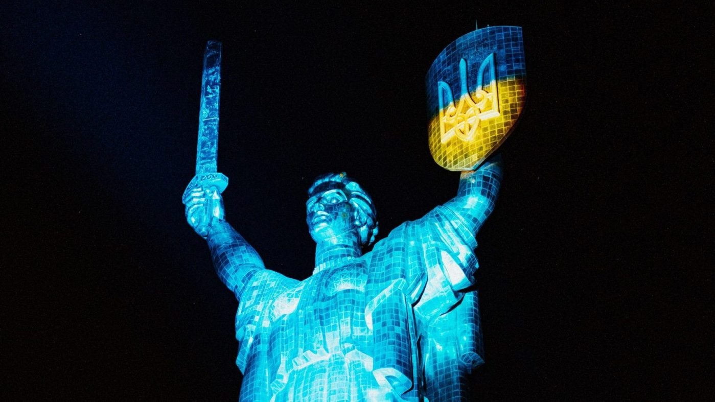 Монумент «Родина-мать» в Киеве, подсвеченный украинскими сине-желтыми цветами ночью — символ стойкости и суверенитета Украины