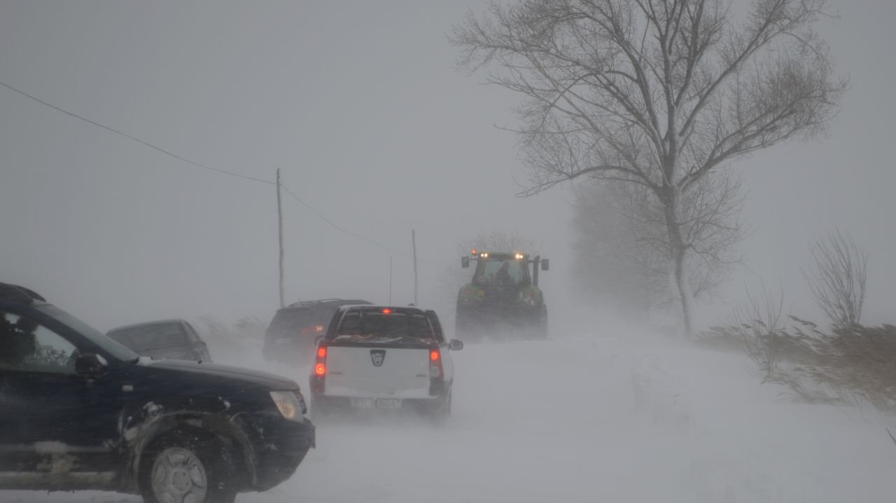 Транспорт застрял в метель, трактор помогает на заснеженной дороге