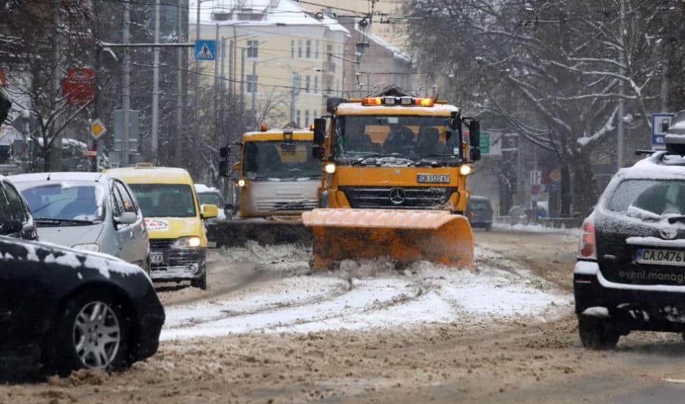 Two yellow snowplows working on Sofia city street with traffic