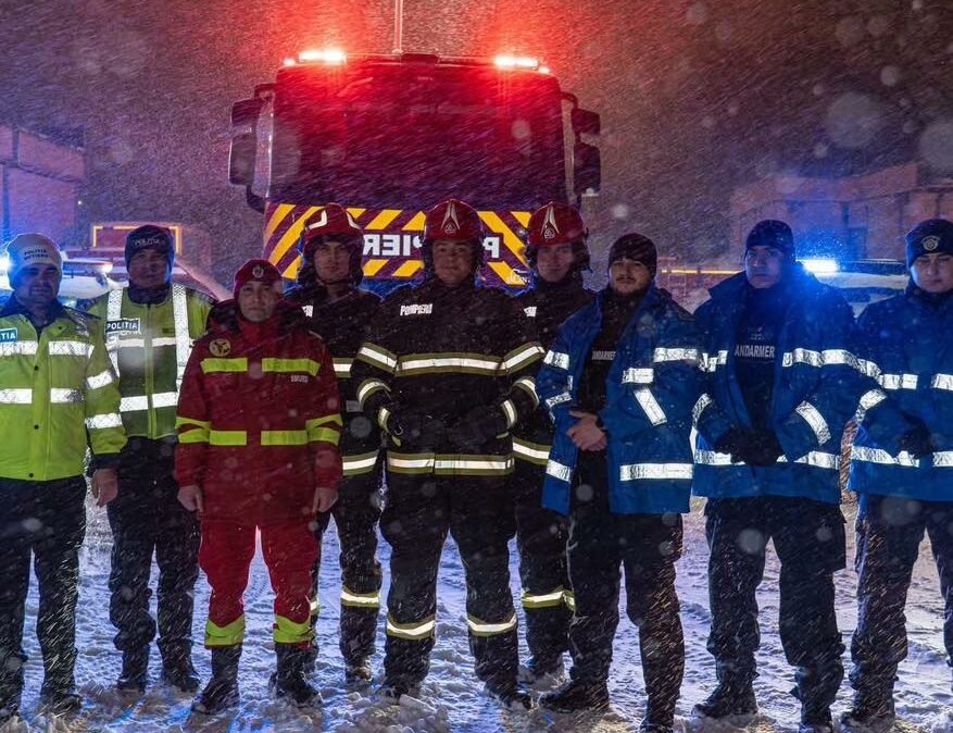 Сотрудники экстренных служб (пожарные, полиция, жандармы) стоят в снежную бурю ночью