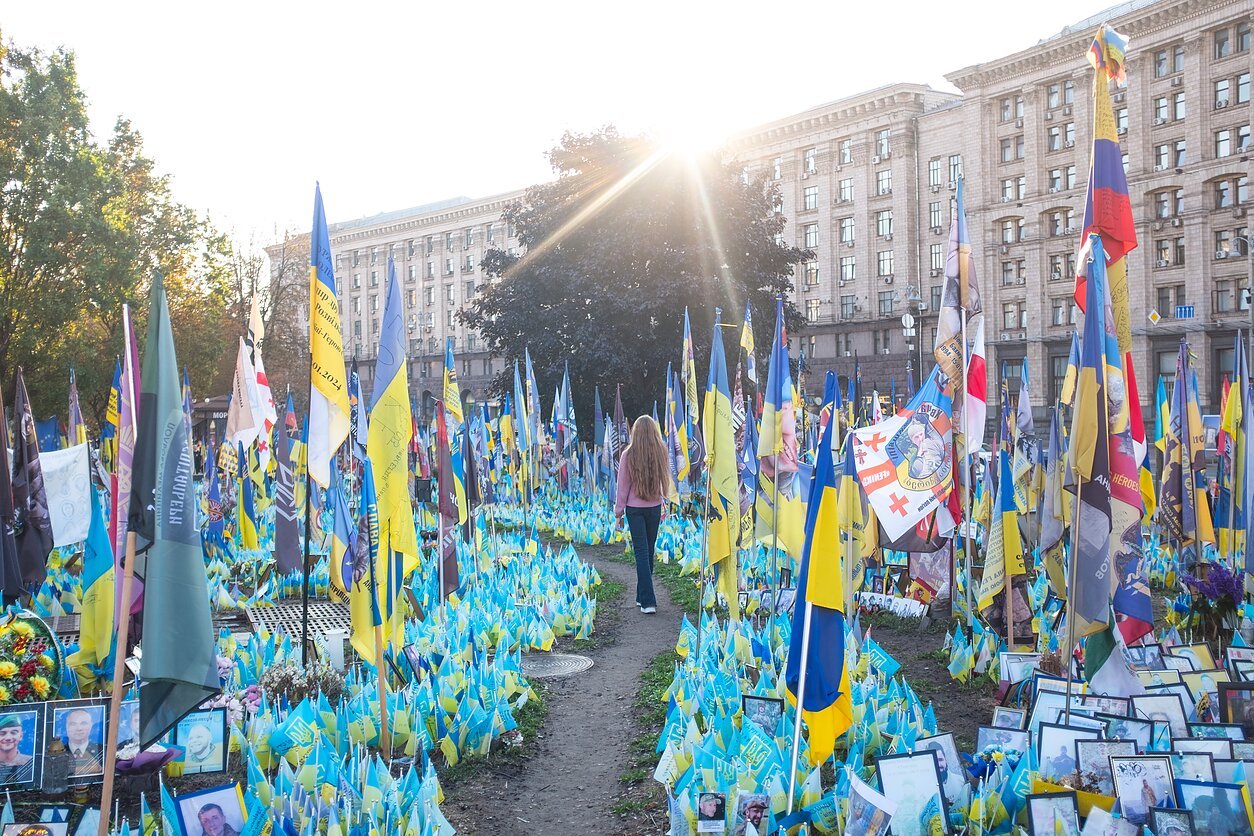 Женщина идет через мемориальное поле с украинскими флагами и фотографиями погибших солдат в Киеве