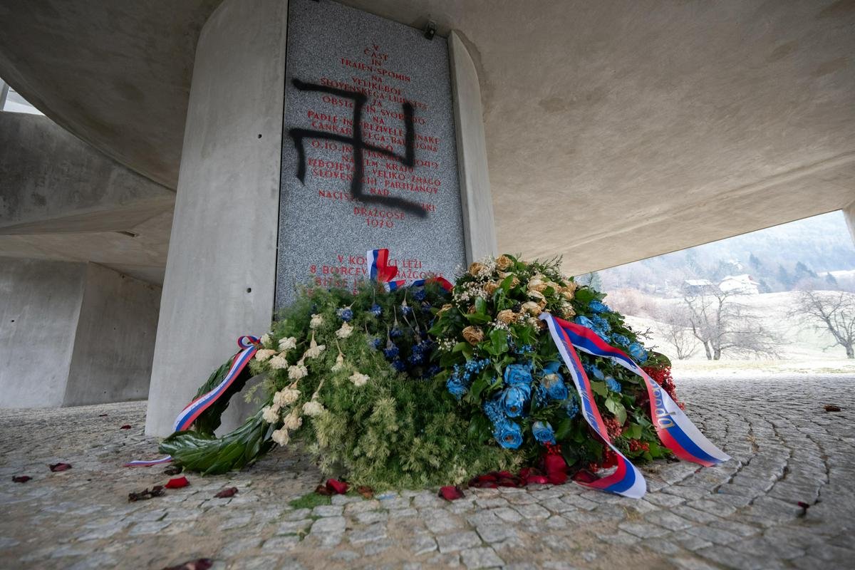 Вид на оскверненный памятник со свежими венками с лентами в цветах Словении у основания