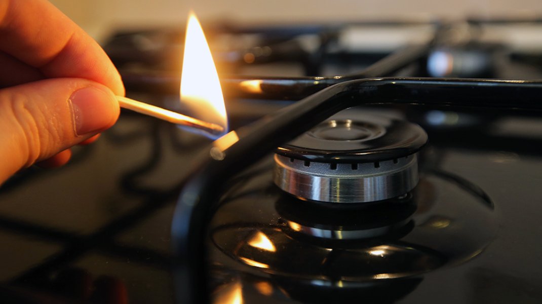 Рука зажигает газовую конфорку спичкой