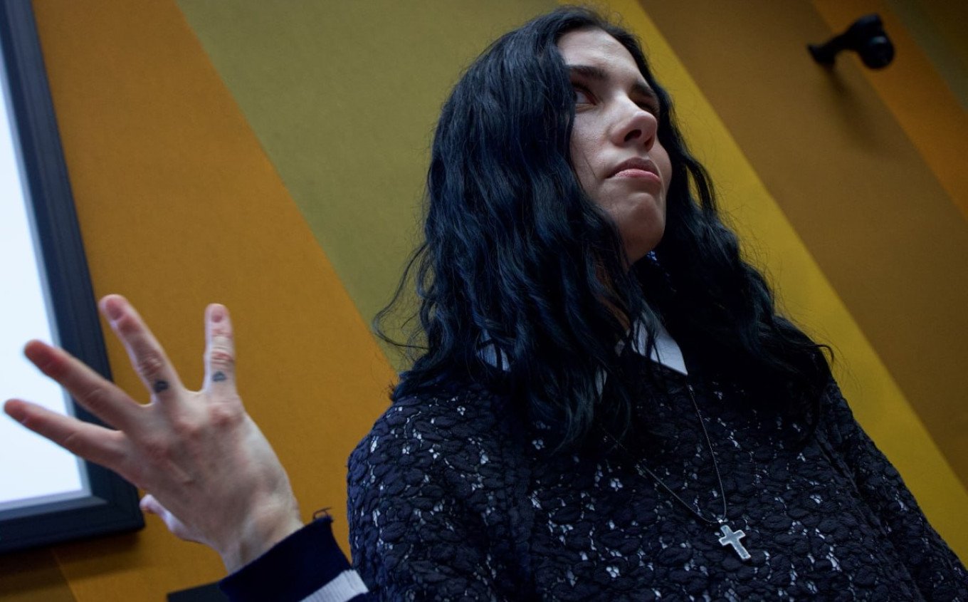 Woman with long dark hair speaking, gesturing with hand