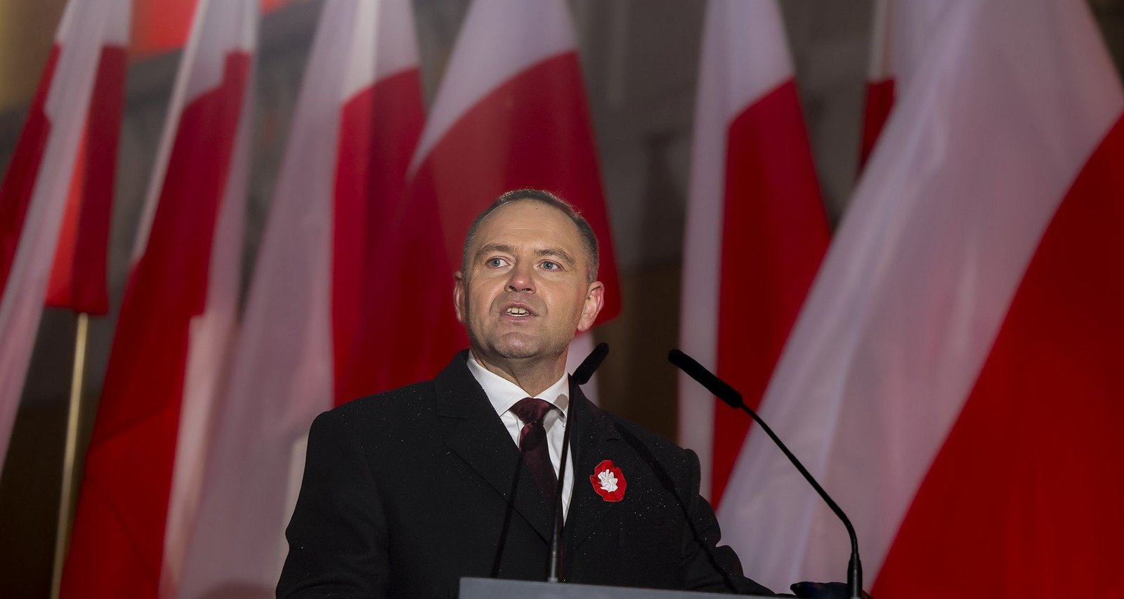 Polish politician speaking with Polish flags in background