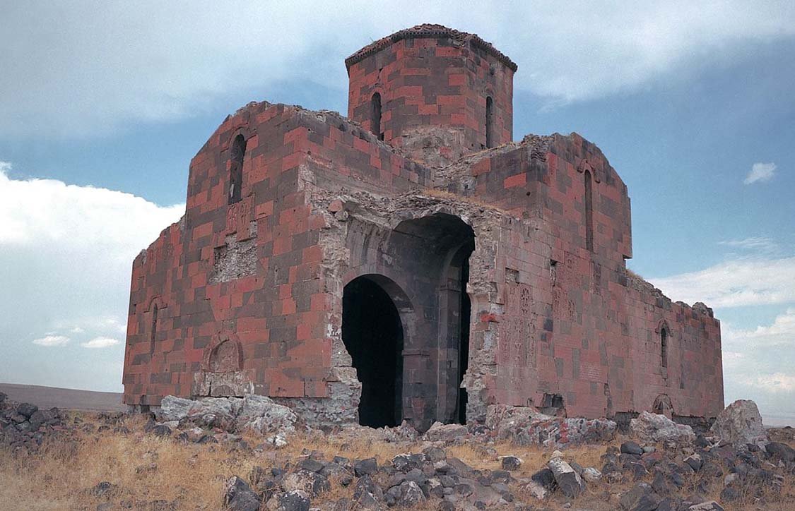 Руины исторической армянской церкви — средневековая архитектура из красного камня на фоне облачного неба