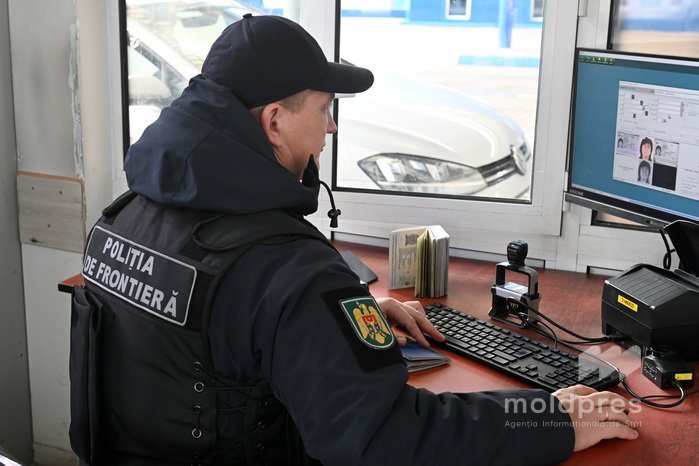 Сотрудник молдавской пограничной полиции на рабочем месте проверяет документы путешественника на компьютере