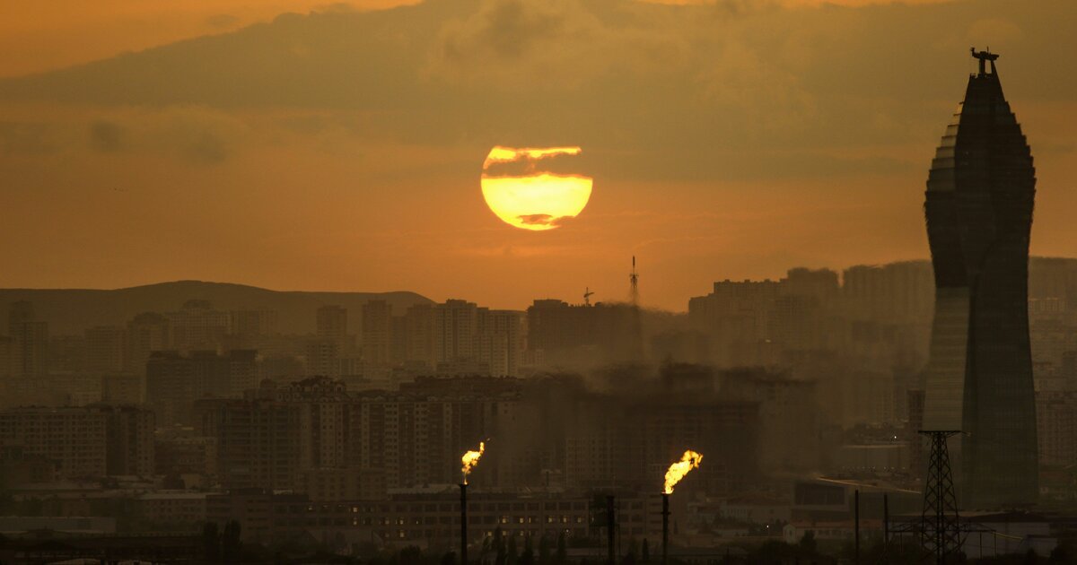 Панорама Баку на закате с горящими газовыми факелами на переднем плане, демонстрирующая присутствие нефтегазовой отрасли в столице Азербайджана