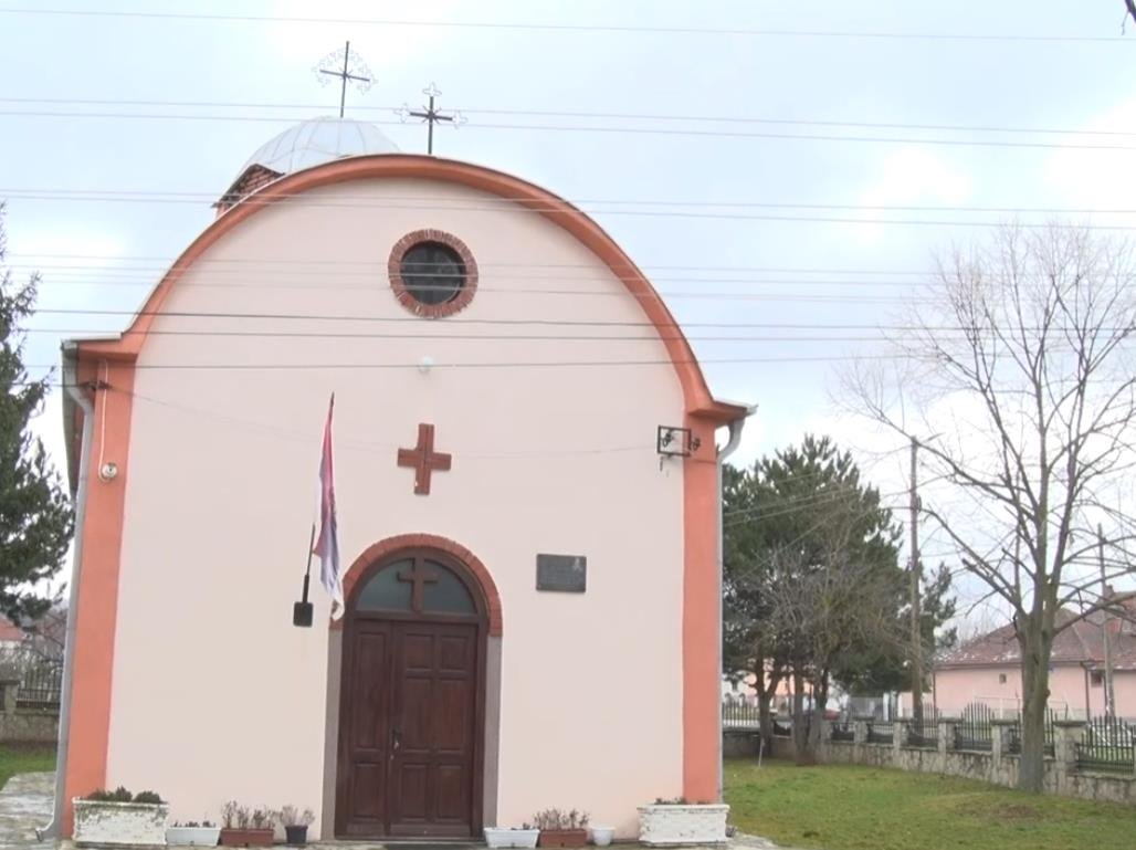 Front view of the small Orthodox church in Gornja Gušterica with pink/white walls and Serbian flag