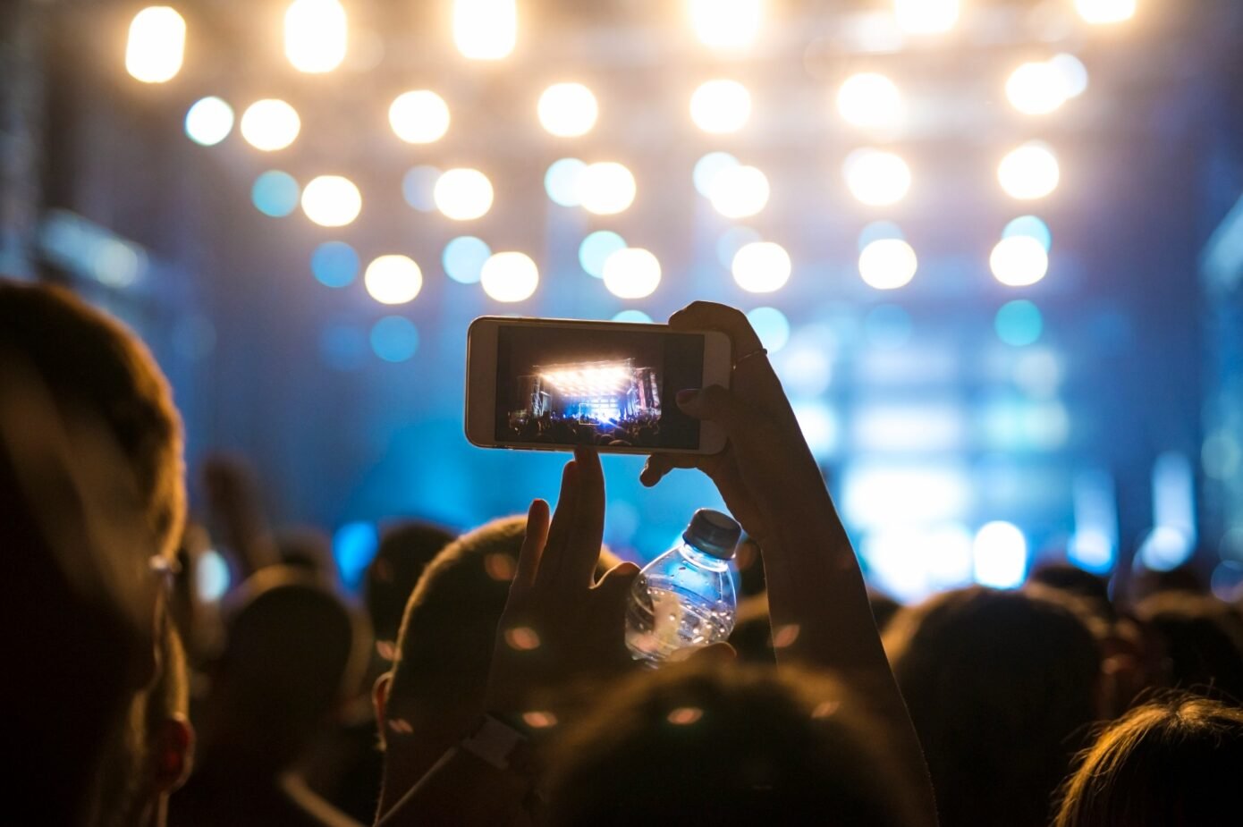Silhouette of person filming concert with phone, bokeh stage lights