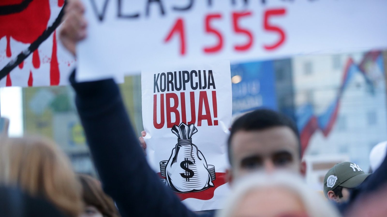 Protest sign reading 'KORUPCIJA UBIJA!' (Corruption kills!) with money bag illustration