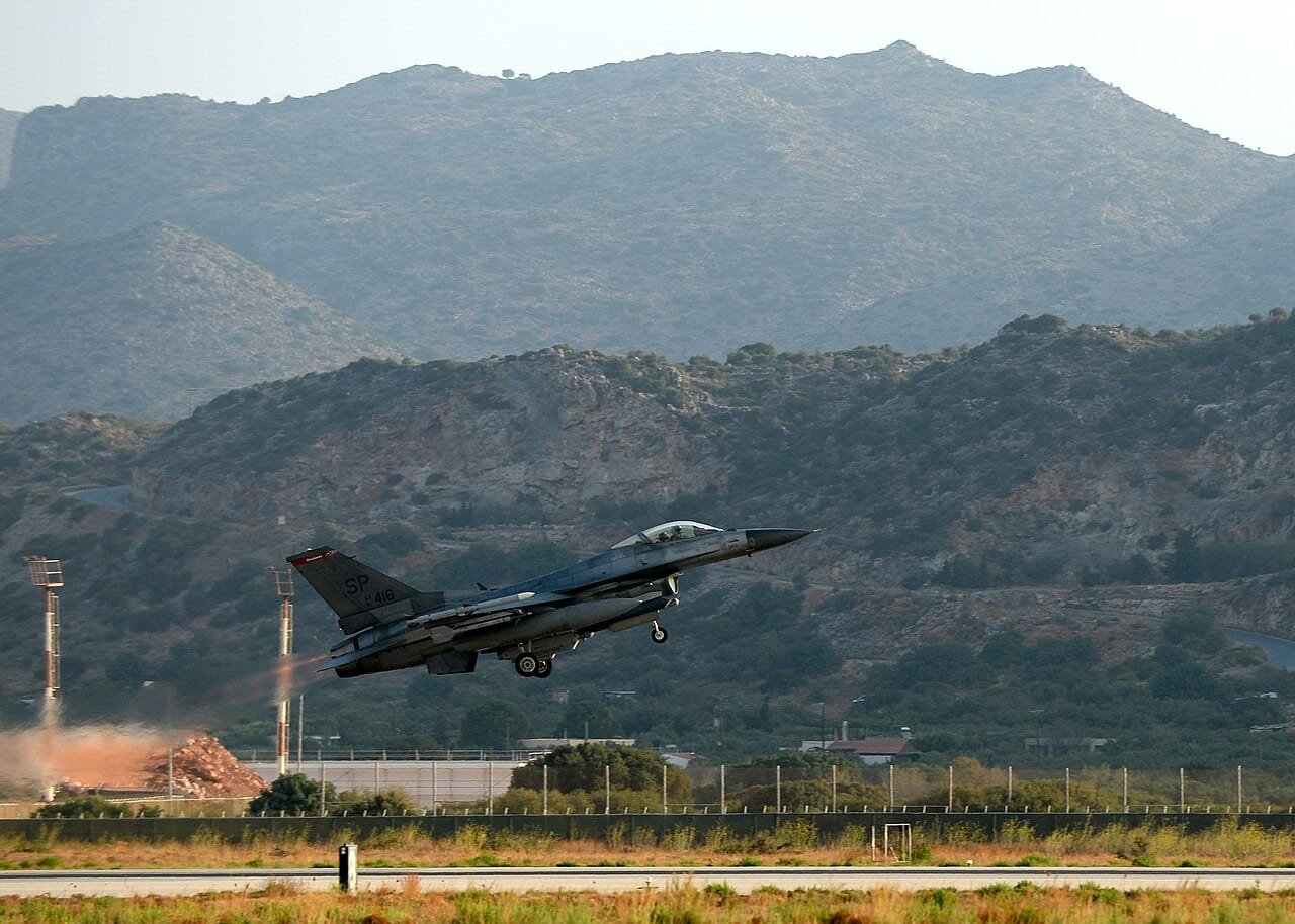 US Air Force F-16 fighter jet taking off from airbase with mountainous terrain in background