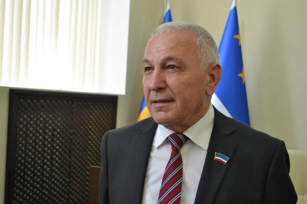 Дмитрий Константинов в деловом костюме на фоне флагов ЕС и Гагаузии