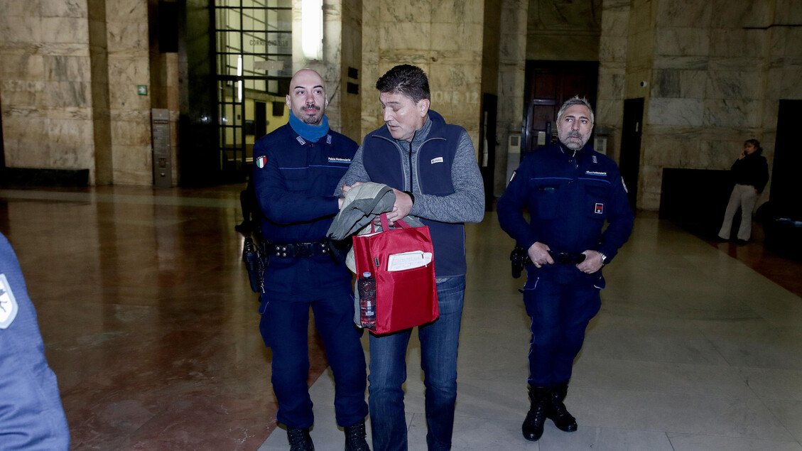 Обвиняемый в сопровождении двух итальянских полицейских в коридоре миланского суда