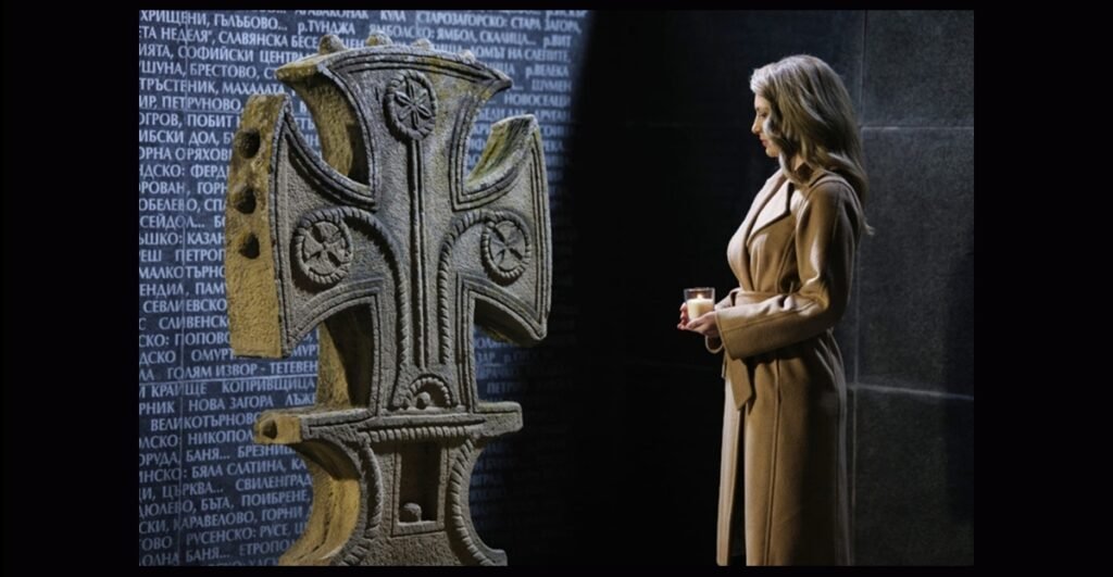 Женщина со свечой у мемориального креста и стены с именами жертв коммунистического режима в Болгарии