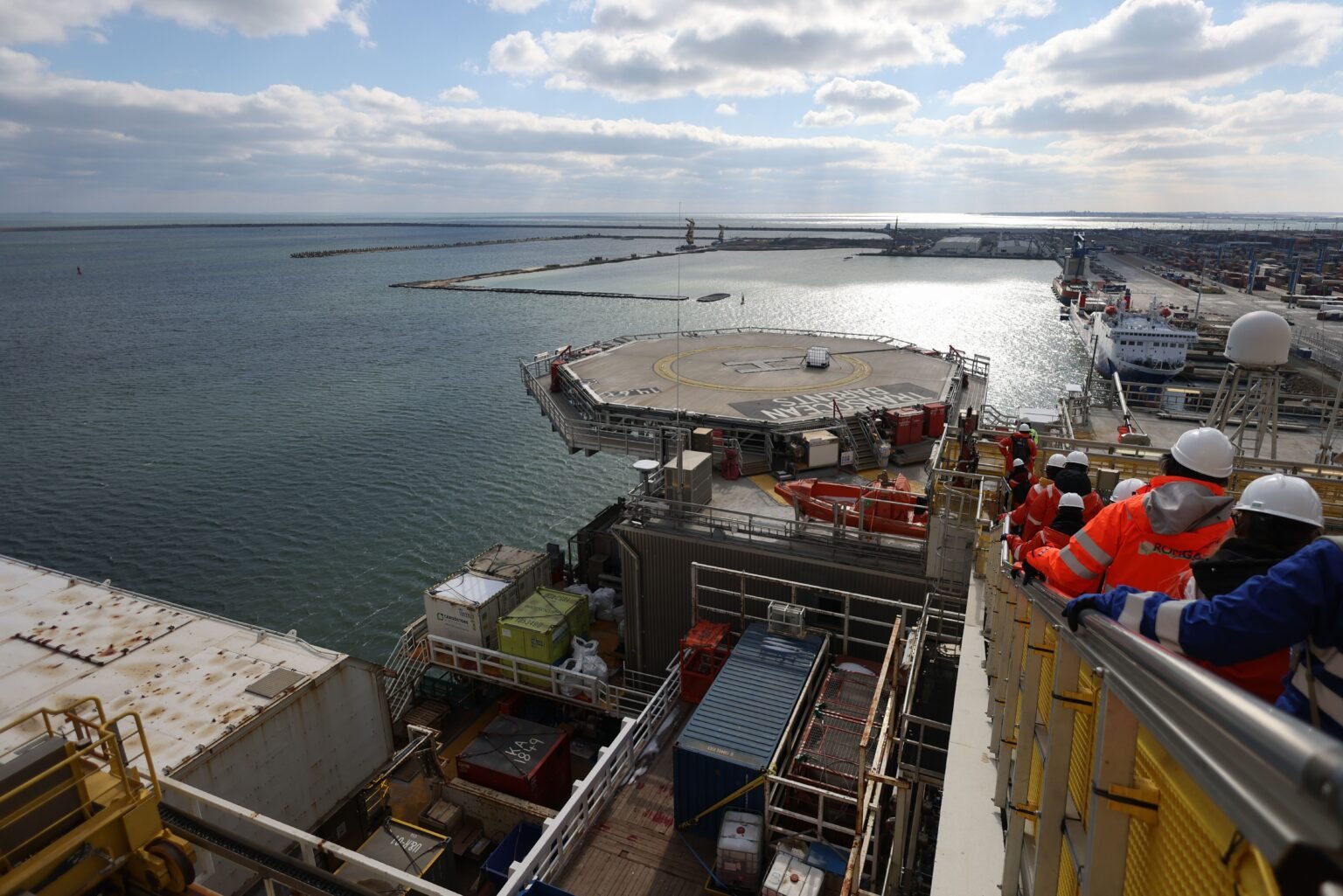 Neptun Deep: почему крупнейший газовый проект ЕС оказался вне защиты НАТО Офшорная нефтегазовая платформа в порту с рабочими в защитном снаряжении, обзорная площадка с видом на вертолётную площадку и морскую инфраструктуру