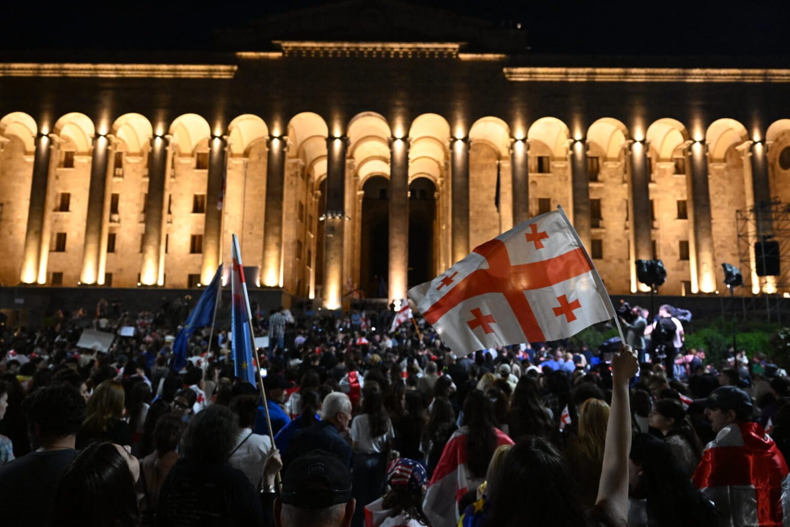 445 дней протестов: как Грузия скатывается к авторитаризму Ночной протест у здания парламента Грузии в Тбилиси, толпа с грузинскими и флагами ЕС при драматическом освещении