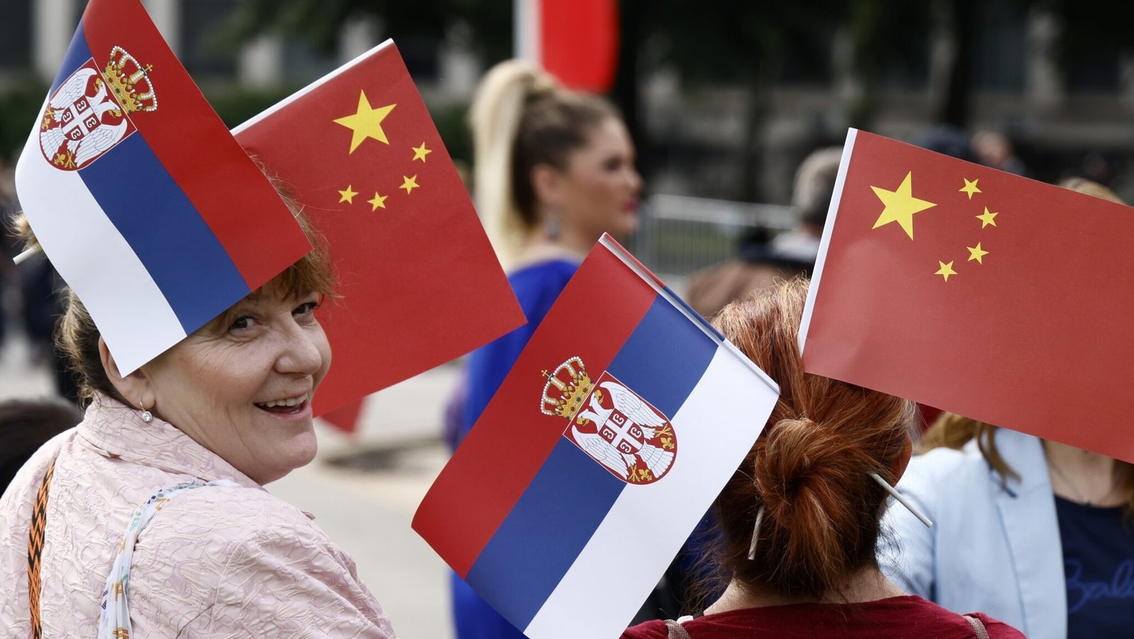 Люди с сербскими и китайскими флагами, символизирующими двусторонние отношения между странами