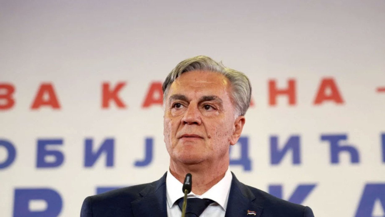 Портрет Синиши Карана на политическом мероприятии с предвыборным фоном