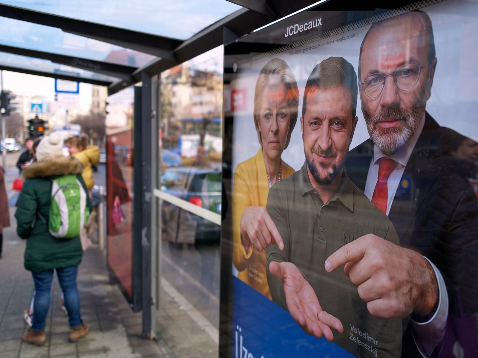 Hungarian government propaganda poster at bus stop featuring Zelensky, von der Leyen, and Weber