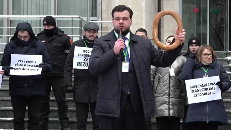 Протест у здания правительства: демонстрант с символическим бубликом и плакатами с критикой PAS и кабинета Мунтяну в день 100-дневной отметки