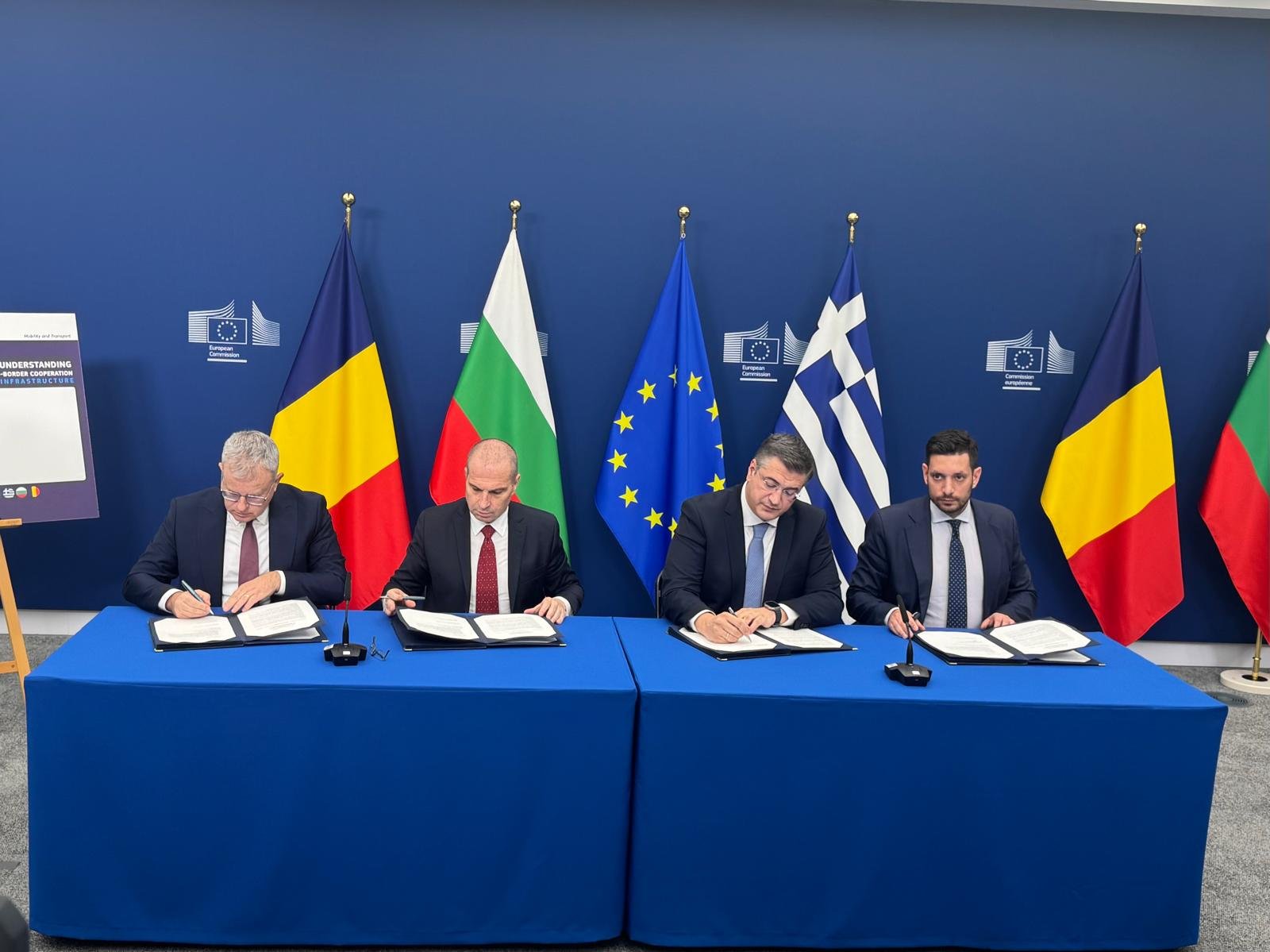 Officials signing agreement at European Commission - Romanian, Bulgarian, Greek and EU flags visible, cross-border infrastructure cooperation
